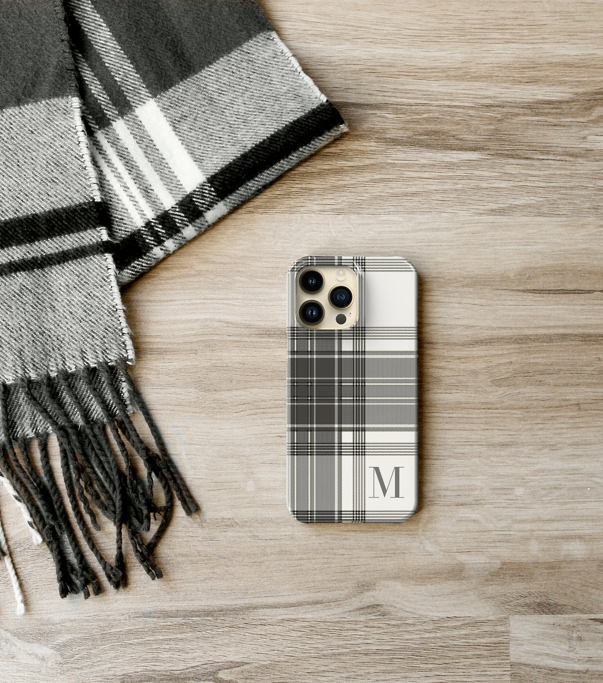 A smartphone with a plaid case and a gray and white striped scarf are placed on a wooden surface.