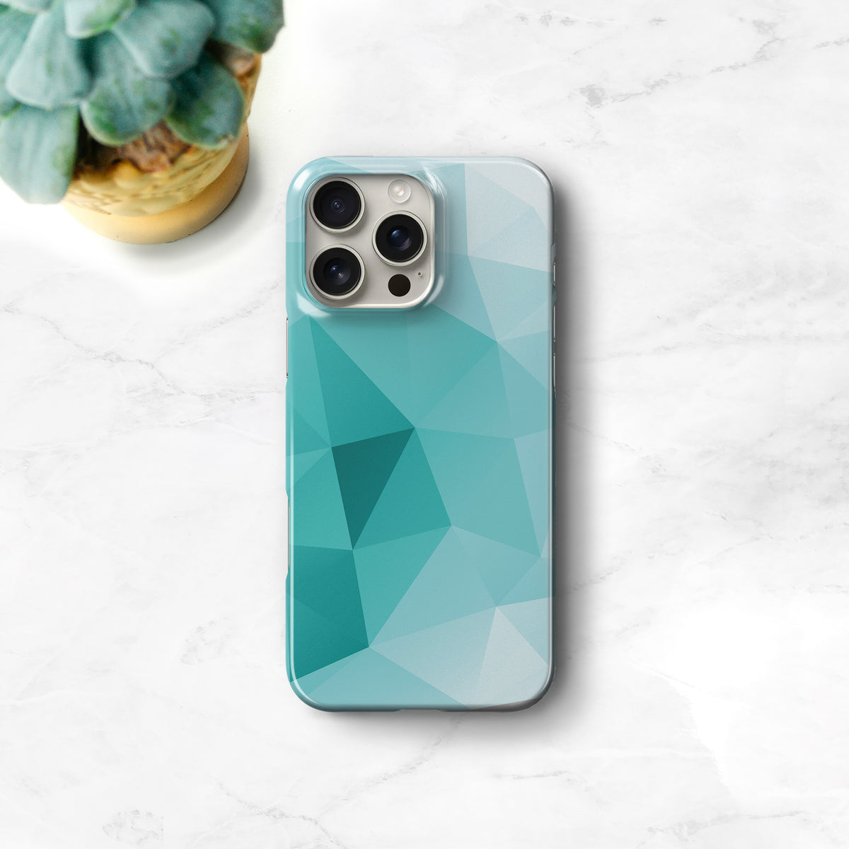 A turquoise-colored phone case with a geometric pattern is placed on a white marble surface, accompanied by a potted succulent plant.