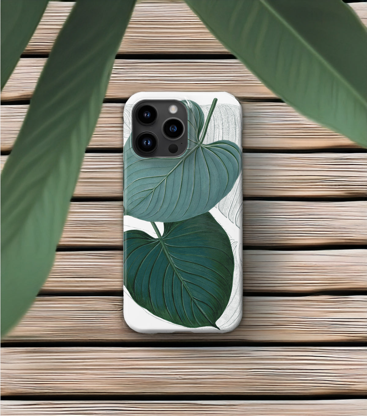 A smartphone case with a leaf design is placed on a wooden surface, with a plant leaf visible in the foreground.