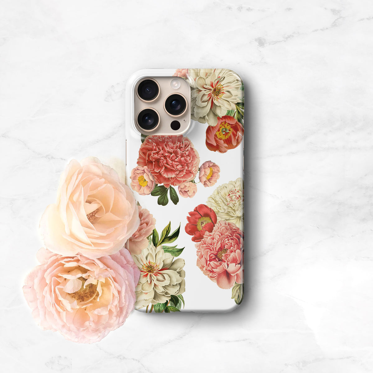A white phone case with a floral design featuring pink and white flowers, including roses and peonies, is displayed on a marble surface.