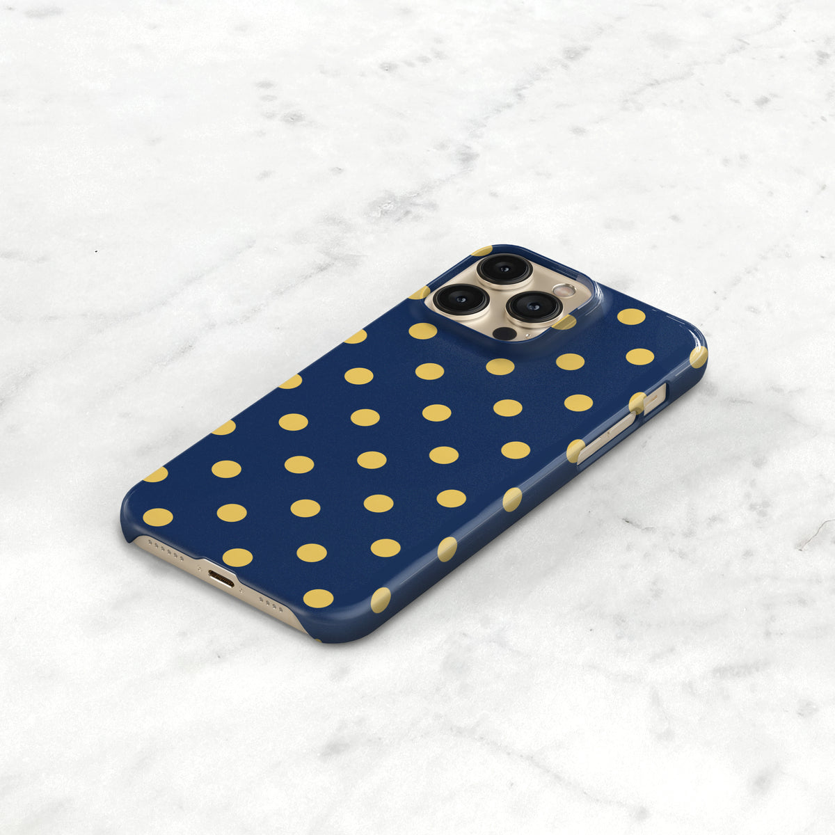 A blue iPhone case with yellow polka dots is placed on a white marble surface.